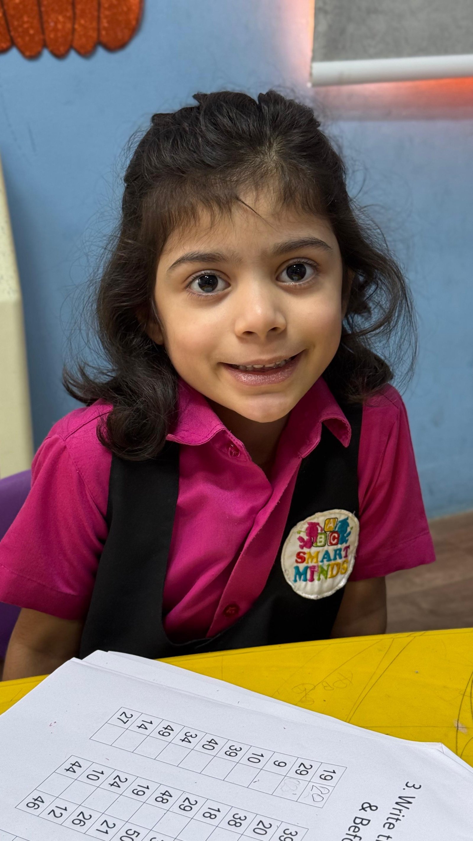 A happy Smart Minds student smiling at her worksheet in a bright classroom