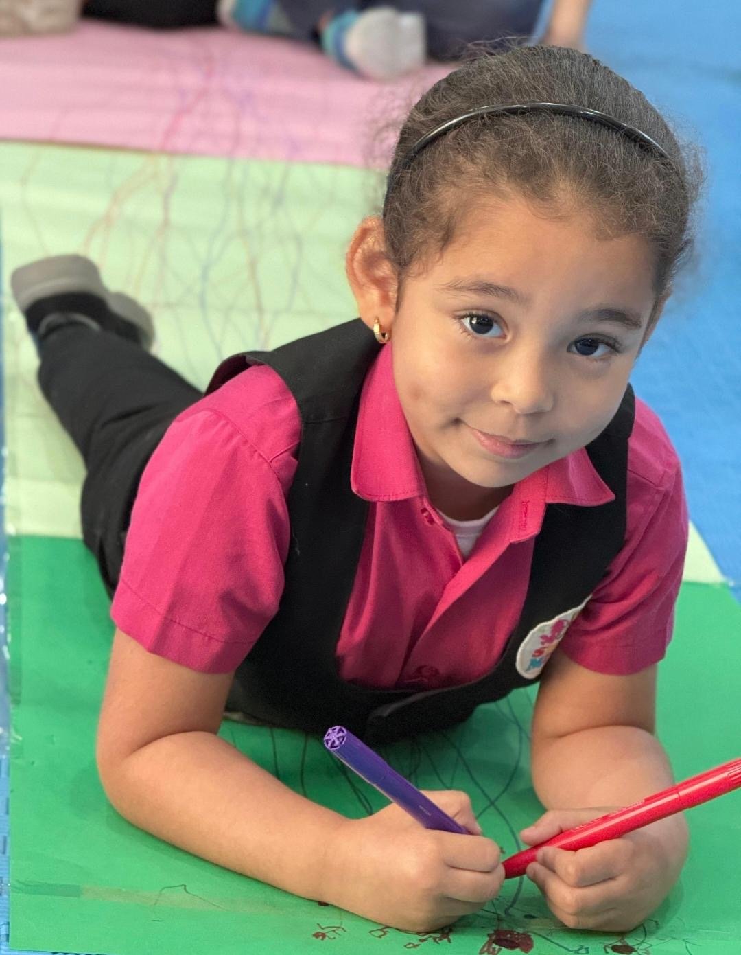 A toddler creating colorful art on the floor at Smart Minds